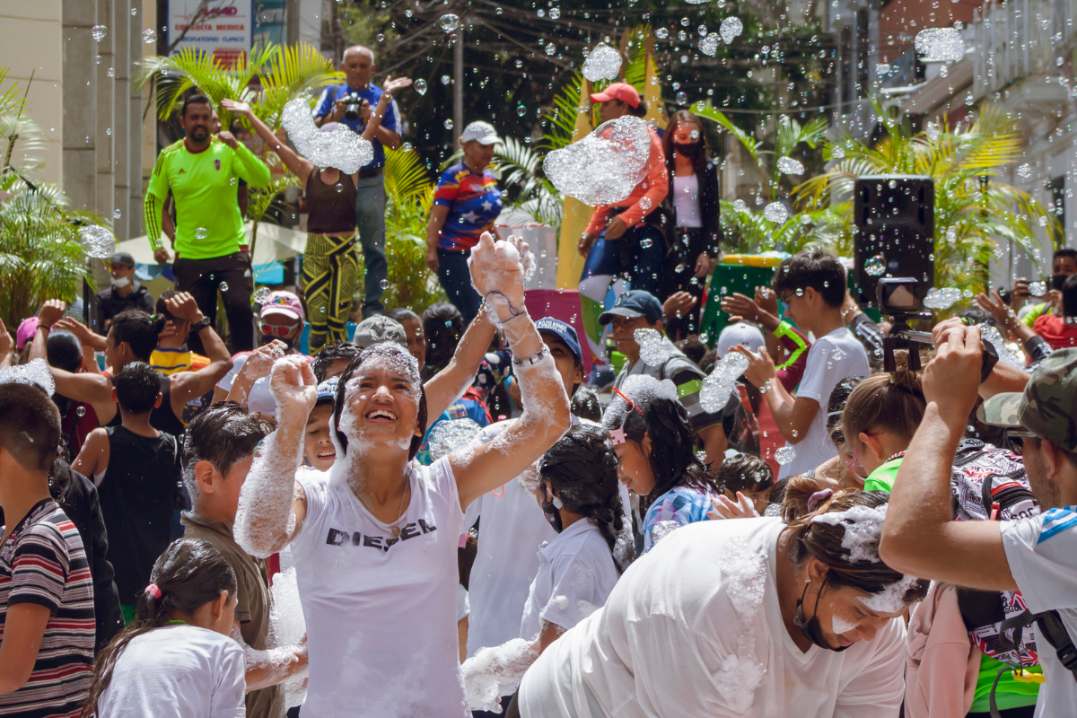 People celebrating at a lively street festival with foam, music, and dancing.